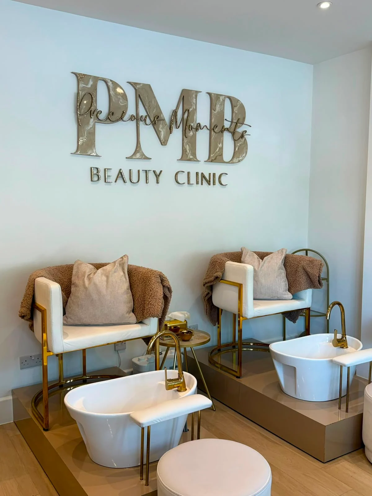 Gold and white pedicure lounge beneath the Precious Moments Beauty Clinic PMB signage at the Banstead clinic